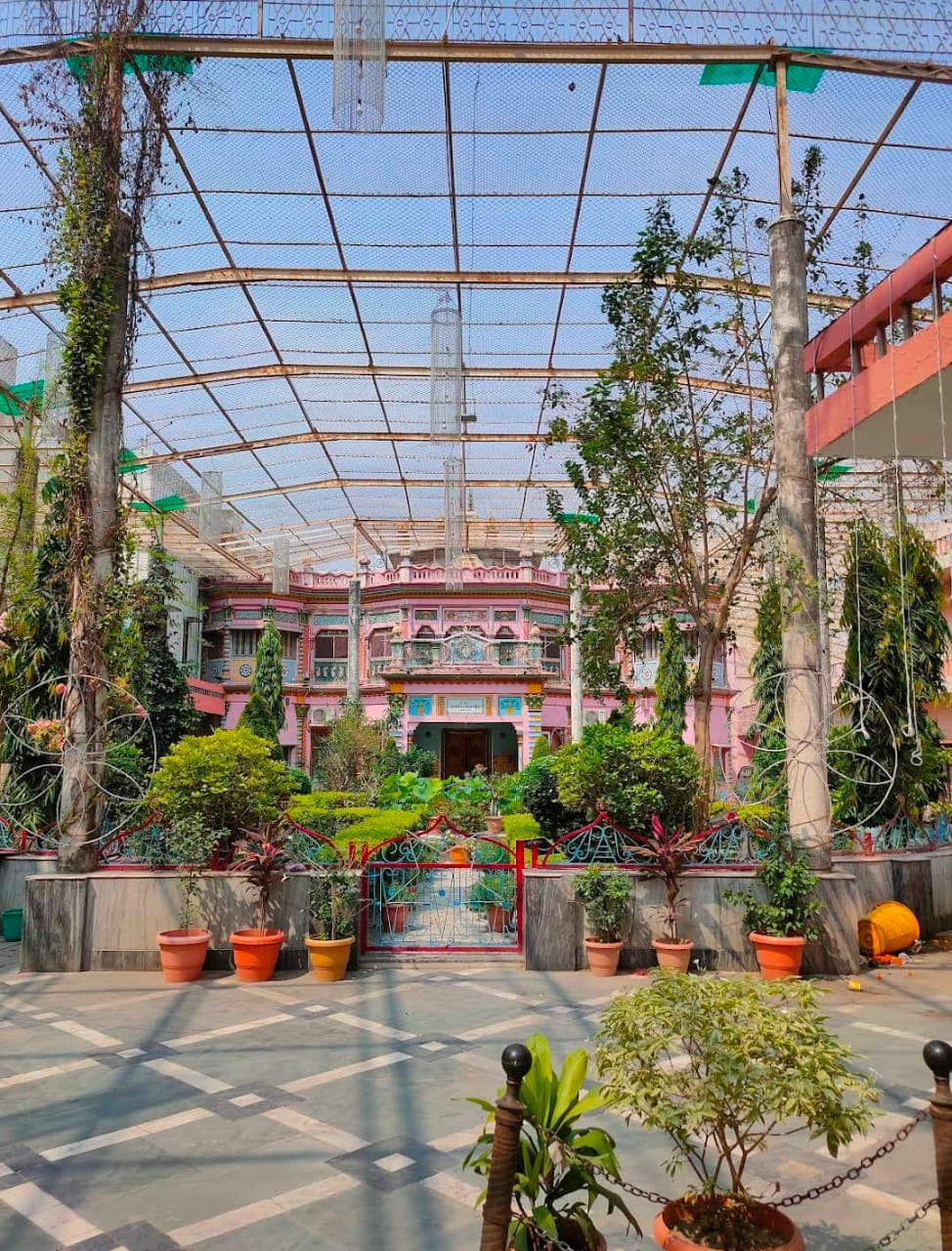 Garden courtyard with potted plants under a netted roof leading to the haveli