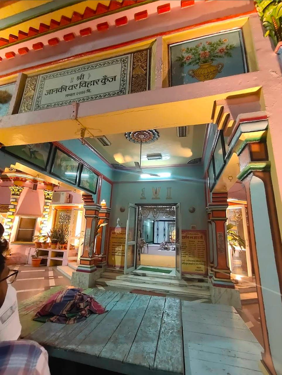 Painted entrance porch of Shri Janaki Var Vihar Kunj with a ceiling fan and framed pictures